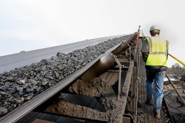 A worker ascends a ramp beside a conveyor belt carrying coal.