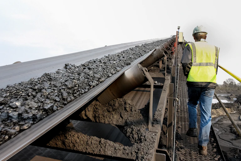 A worker ascends a ramp beside a conveyor belt carrying coal.
