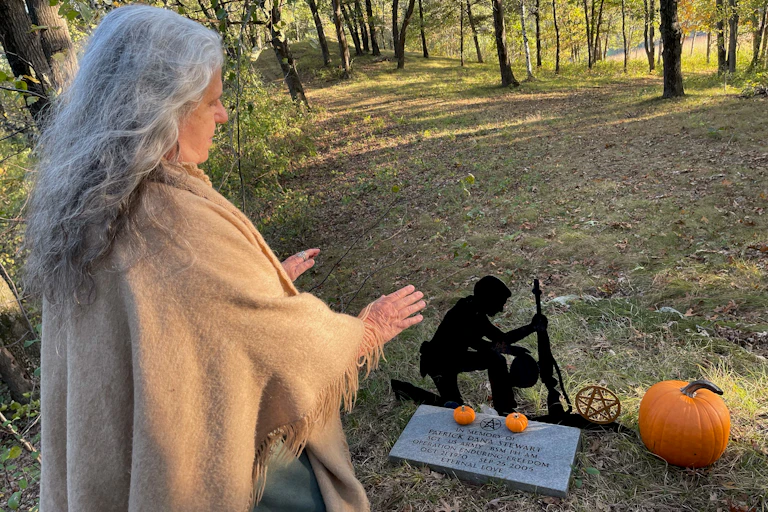 Wiccan high priestess performs ceremony in front of military grave inscribed with a pentagram