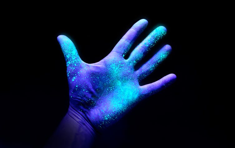 Uma mão sob a luz ultravioleta brilhando em muitos lugares.