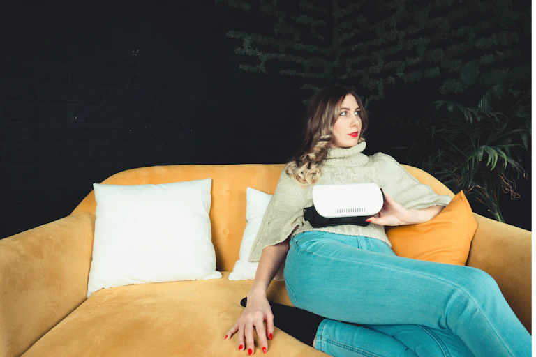 Une femme est assise sur un sofa jaune, un appareil de RV à la main