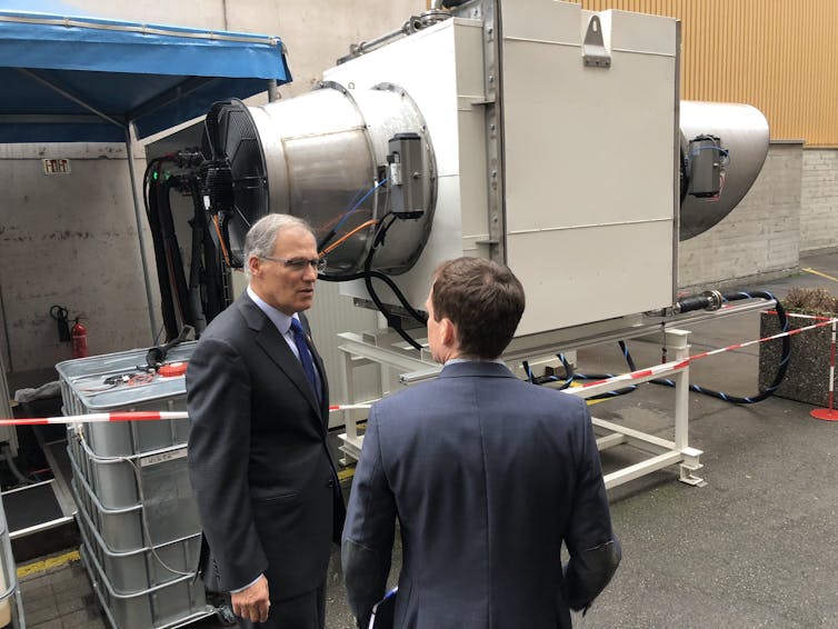 A machine with an intake and tubes behind two men talking.