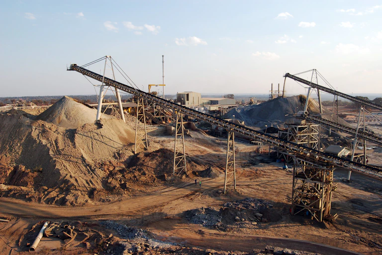 Two men walk under a conveyor belt at an open cast mine in Zambia