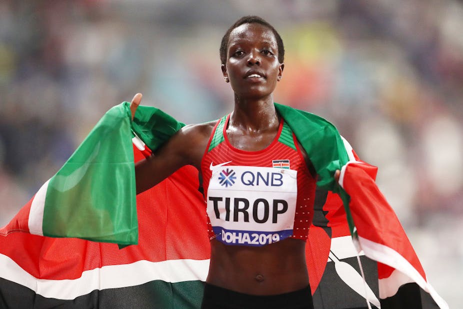 A woman wearing runner's gear and bib, with Kenya flag around her shoulders