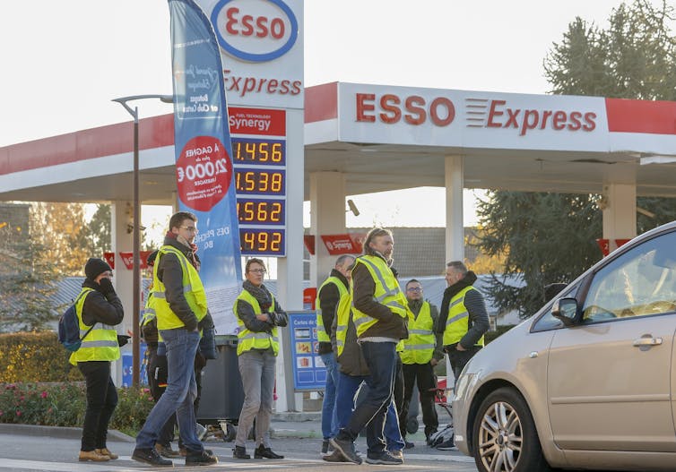Protesters stand in yellow high-visibility jackets outside a petrol station forecourt.