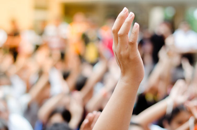 Hands raised at a large outdoor gathering of people.