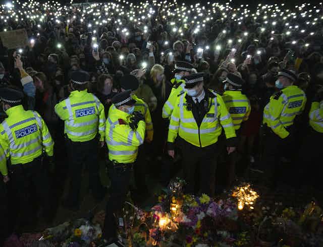Women shine their phone lights on a line of police at a vigil for Sarah Everard in Clapham, March 2021.