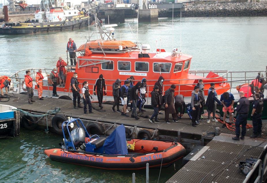 Des migrants sont escortés alors qu'ils débarquent d'un navire de la Société Nationale de Sauvetage en Mer (SNSM) à Calais,  le 15 septembre 2021, après avoir été secourus par un navire de la SNSM alors que leur bateau gonflable se remplissait d'eau dans la Manche.