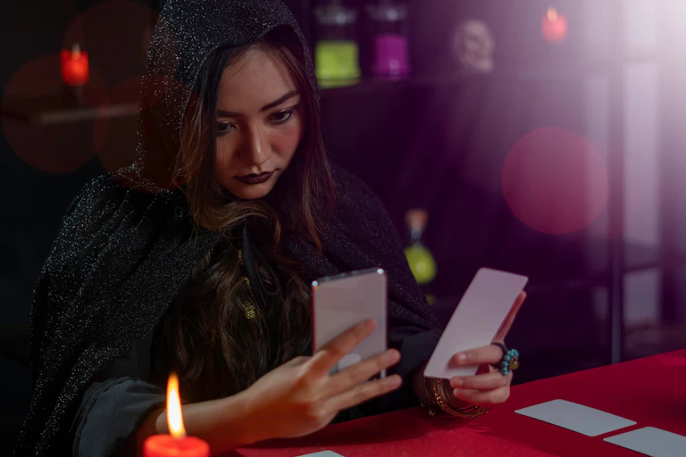 Woman dressed as a witch holding a phone and a tarot card