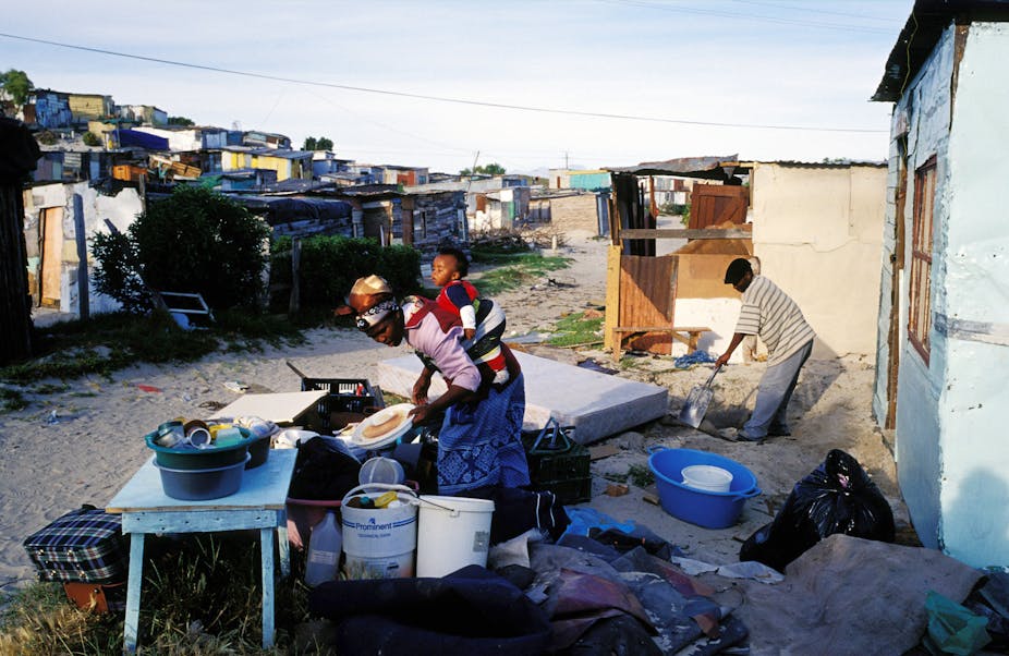 A woman with her baby collects her household goods in front of her newly built shack.