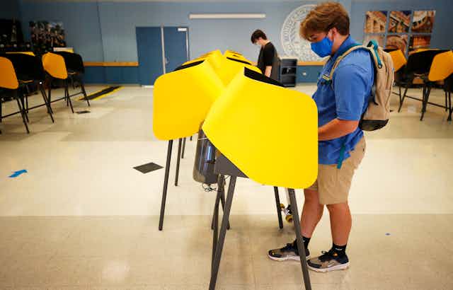 A college student wearing a mask votes at a poll.