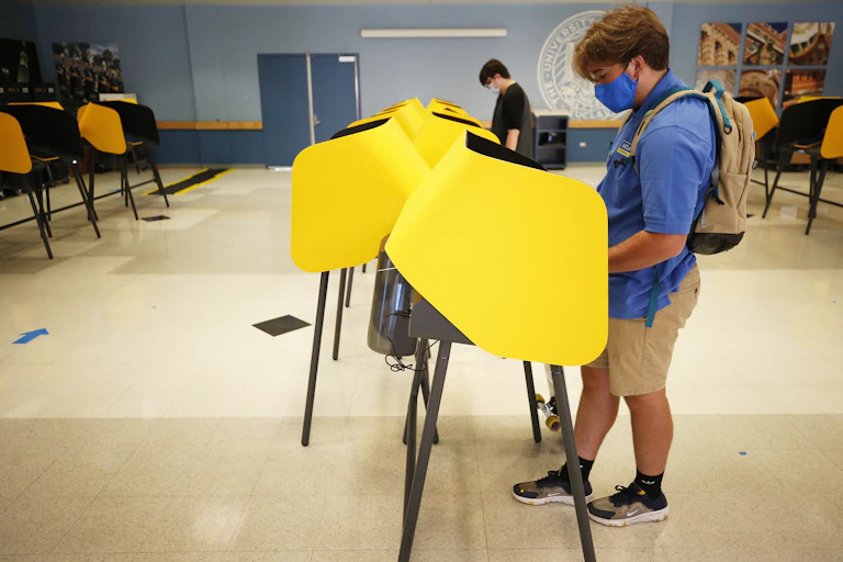 A college student wearing a mask votes at a poll.