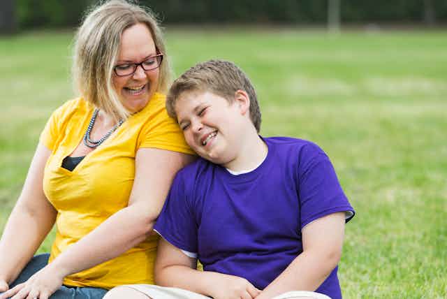 Mother and son sit on grass laughing together