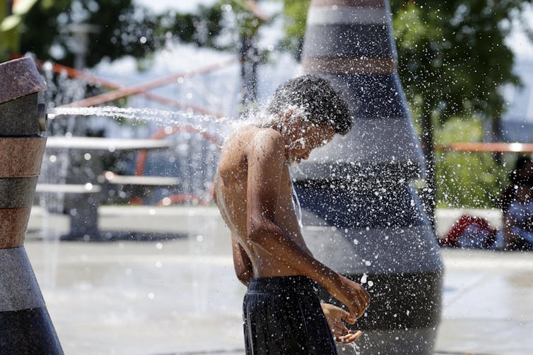 Boy in bathing suit standing next to fountain.