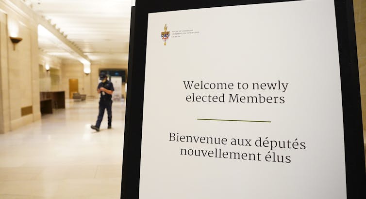 A guard walks in the background behind a message board welcoming newly elected MPs.