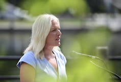 A blonde woman in a blue shirt speaks into a microphone