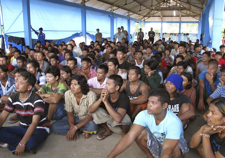 Dozens of people sit on the floor in a large tent.