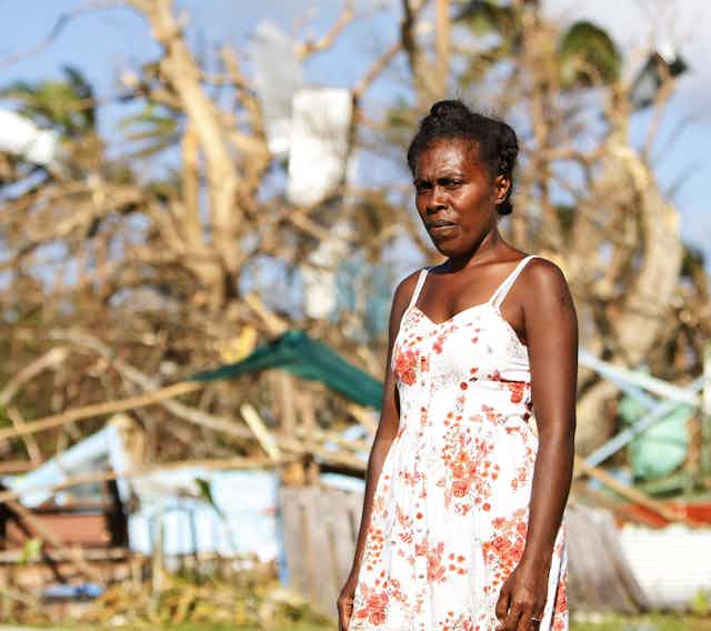 A principal stands in front of her destroyed home in Vanuatu.