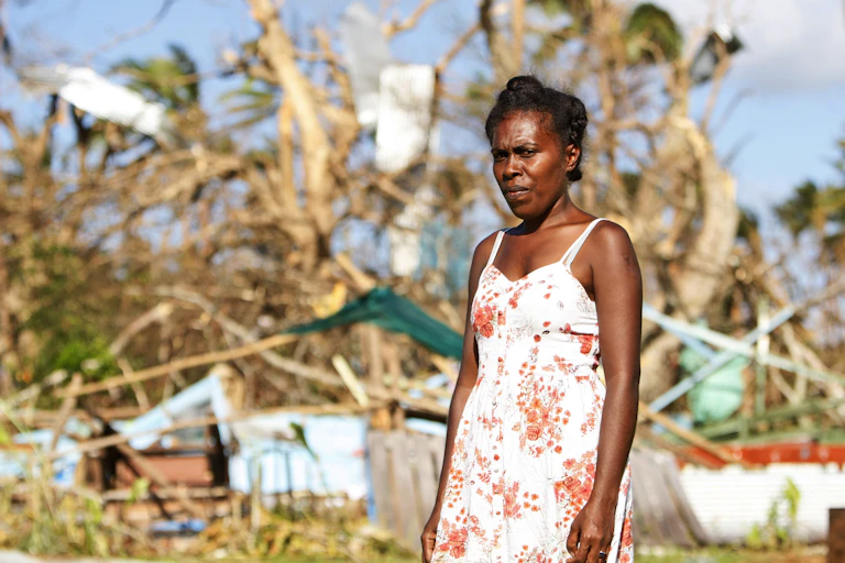 A principal stands in front of her destroyed home in Vanuatu.