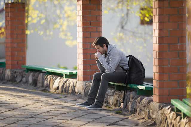 Male university student sitting on bench with backpack.