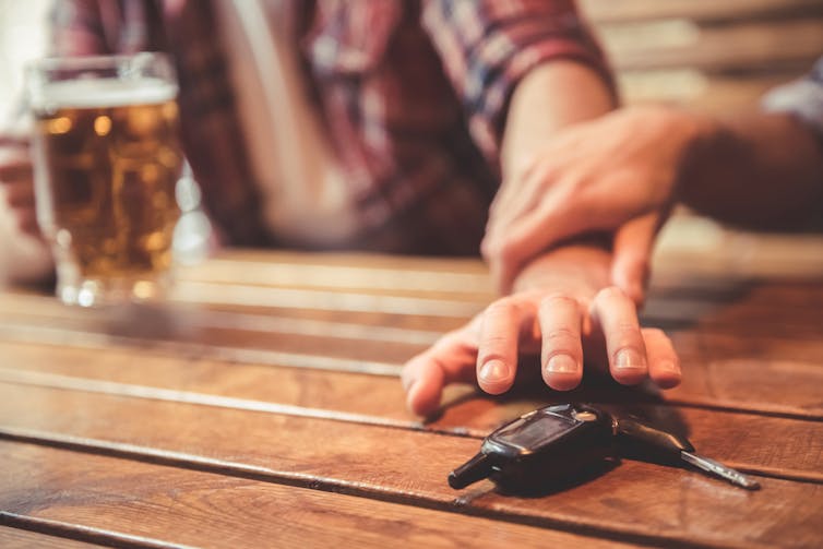 Man drinking beer about to grab car keys, friend holding back arm