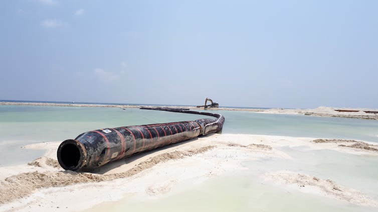 A black pipe lies across a sandy beach