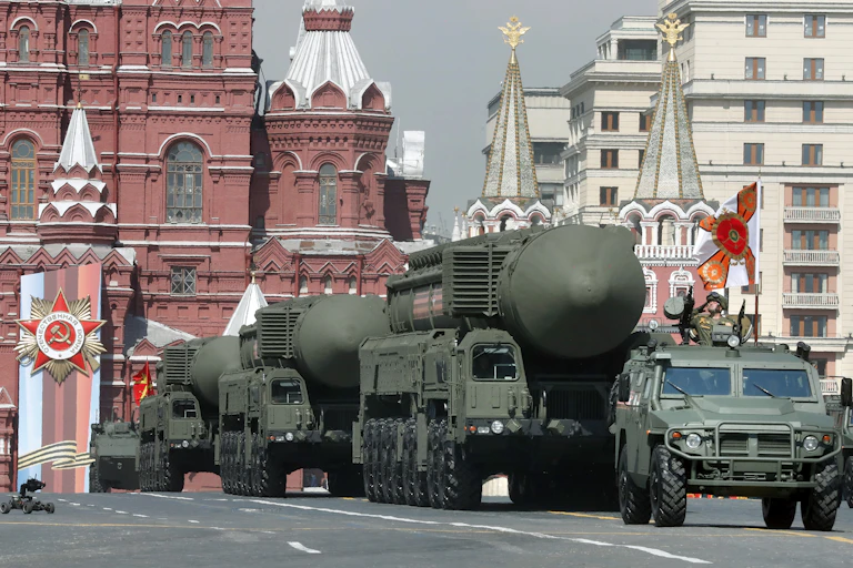 An armoured military van drives ahead of three large trucks, each carrying enormous nuclear missile