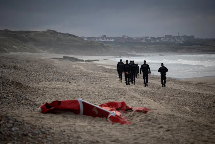 Des policiers français patrouillant sur une plage dans le nord de la France, passent devant l’épave d’un bateau pneumatique utilisé par les migrants qui tentent de traverser la Manche vers l’Angleterre, le 16 octobre 2021