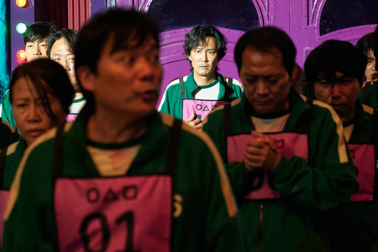 Characters in the TV show Squid Game line up looking tired and haunted.