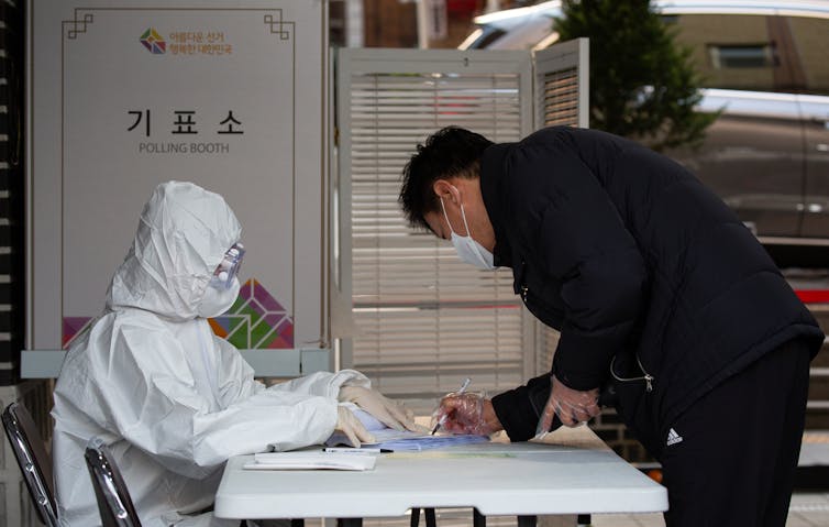 A self-isolating man voting at a polling station, with officials wearing full PPE