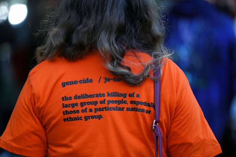 A woman wears an orange shirt printed with the definition of genocide printed on the back