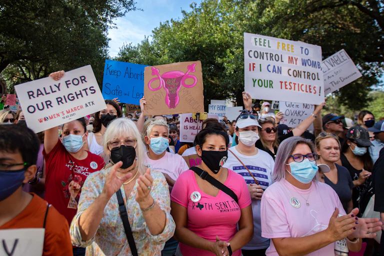 Hundreds of marchers, waving protest signs at the State Capitol building in Austin, urge Texans to oppose the state's new abortion law.