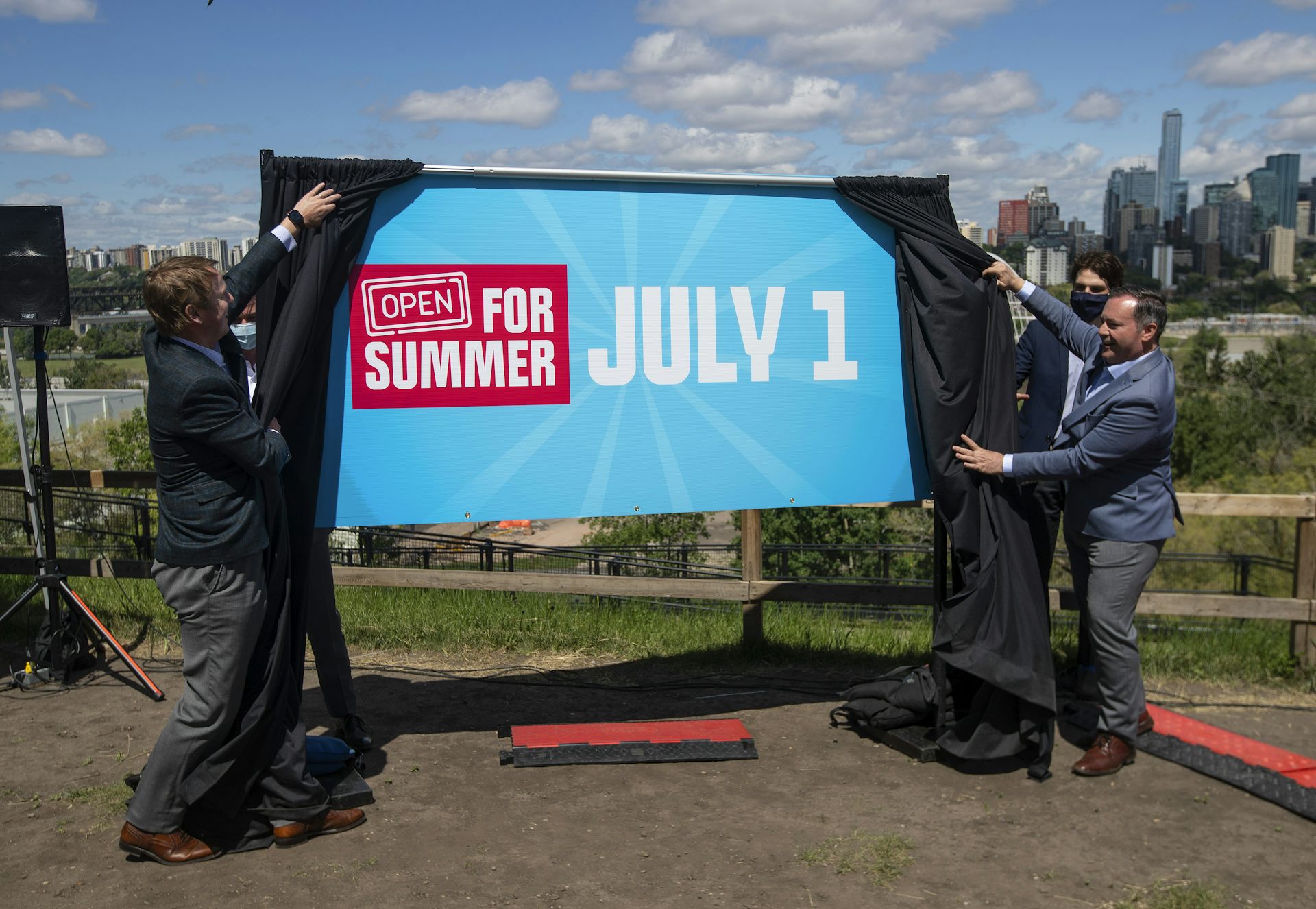 Men unveil a sign that reads 'open for summer July 1'