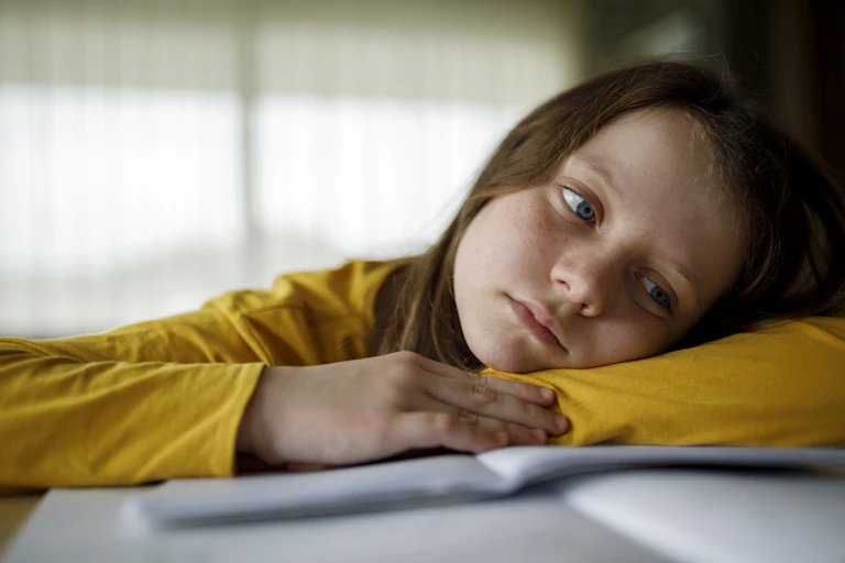 Bored girl resting her head on her arm while struggling to do homework