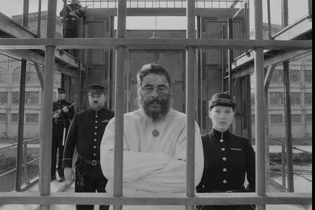 Man in a straight jacket flanked by guards. 