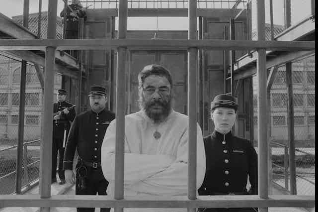 Man in a straight jacket flanked by guards. 