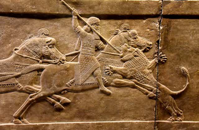 A stone carving of an Assyrian king on horseback stabbing a lion with a spear.