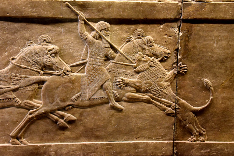 A stone carving of an Assyrian king on horseback stabbing a lion with a spear.
