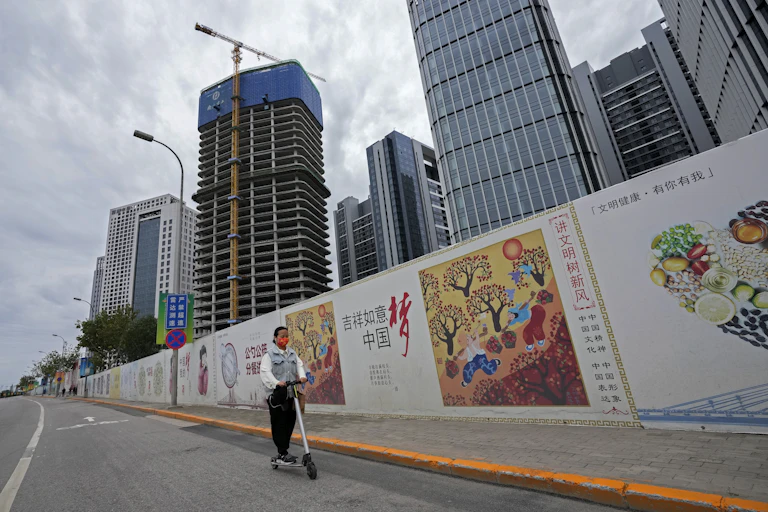 Young woman on scooter riding along Beijing street. past Chinese government "China Dream" billboards.
