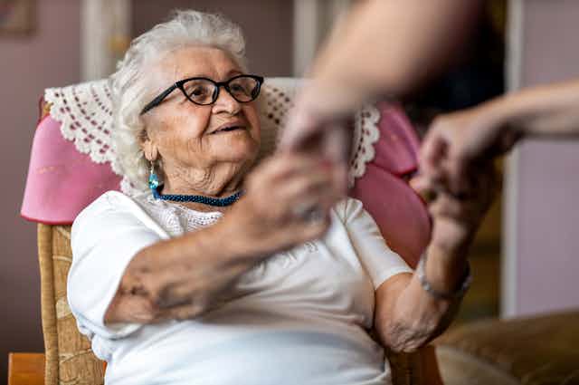Elderly lady sitting in armchair with carer holding her hands
