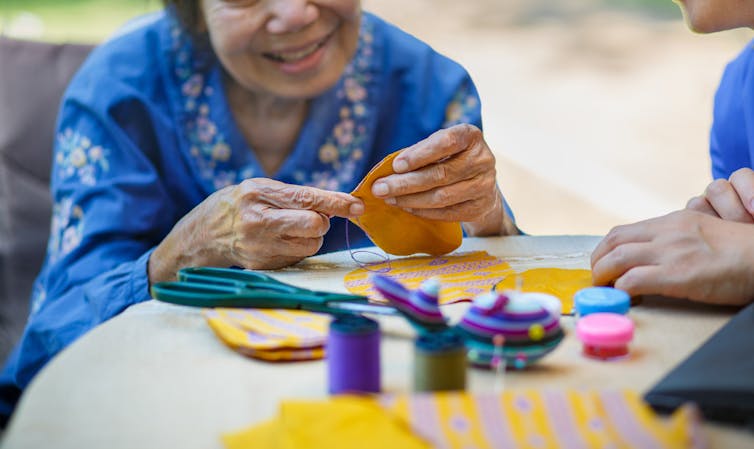 Elderly lady doing crafts with a carer, outside at a table