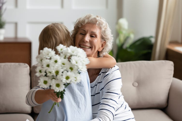 Elderly woman with bunch of flowers hugging child