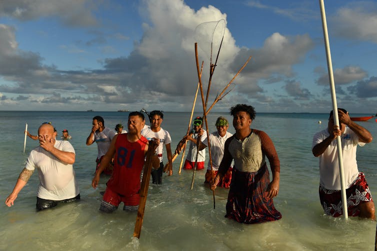 People stand in water with spears