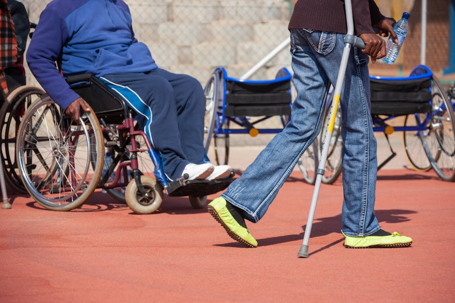 A man sitting on a wheelchair and a women walking with crutches.