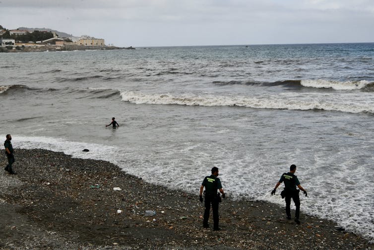 Security officials at a beach, staring at a man swimming in the sea.