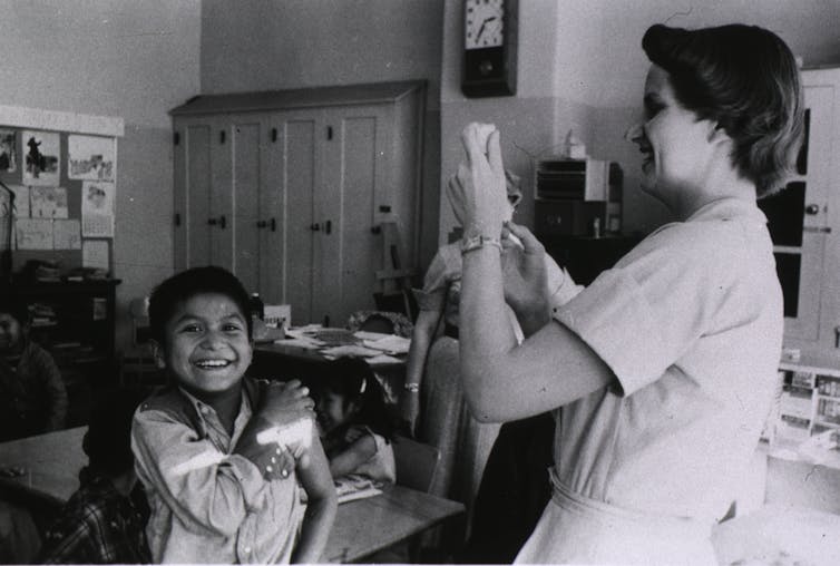 Smiling boy rolls up his sleeve to get a shot from a nurse