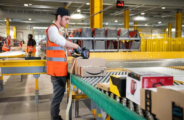 A warehouse worker in a bright orange vest scans a package at an Amazon fulfilment centre