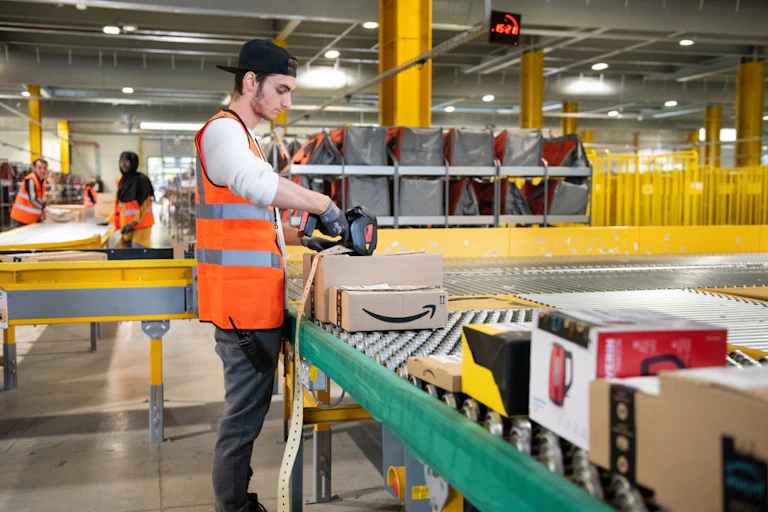 A warehouse worker in a bright orange vest scans a package at an Amazon fulfilment centre