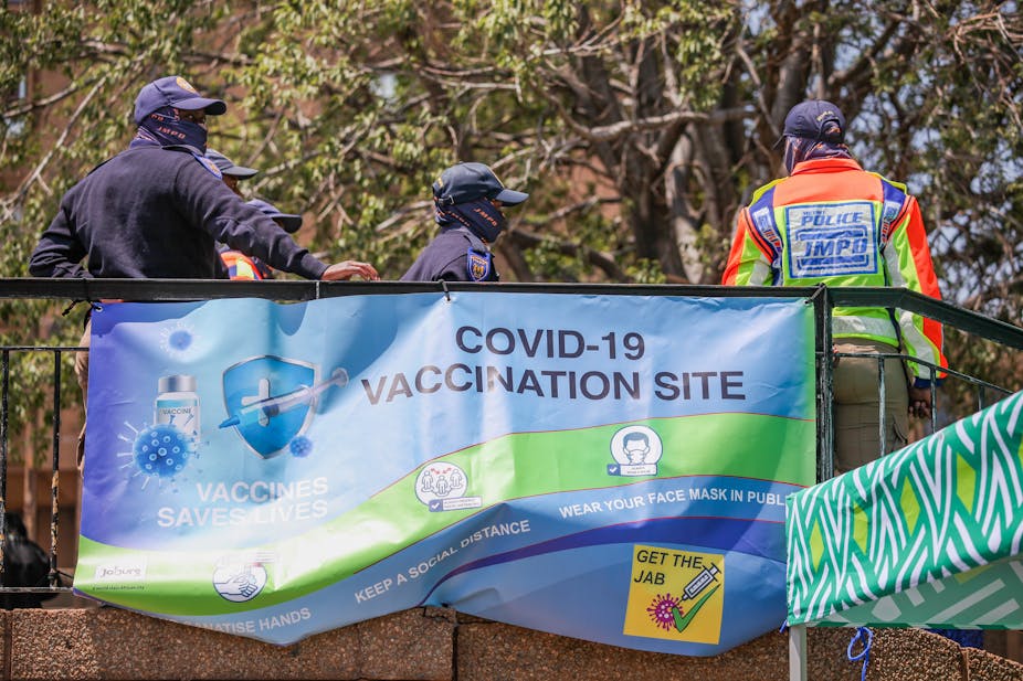 Police in uniform standing in front of a banner indicating a vaccination site