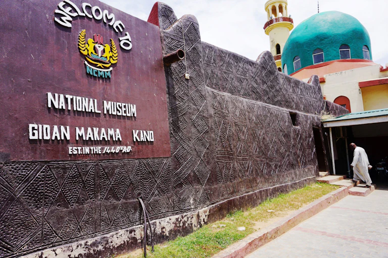 Exterior of a building with a sign indicating it is a museum; a man walks up steps at the entrance